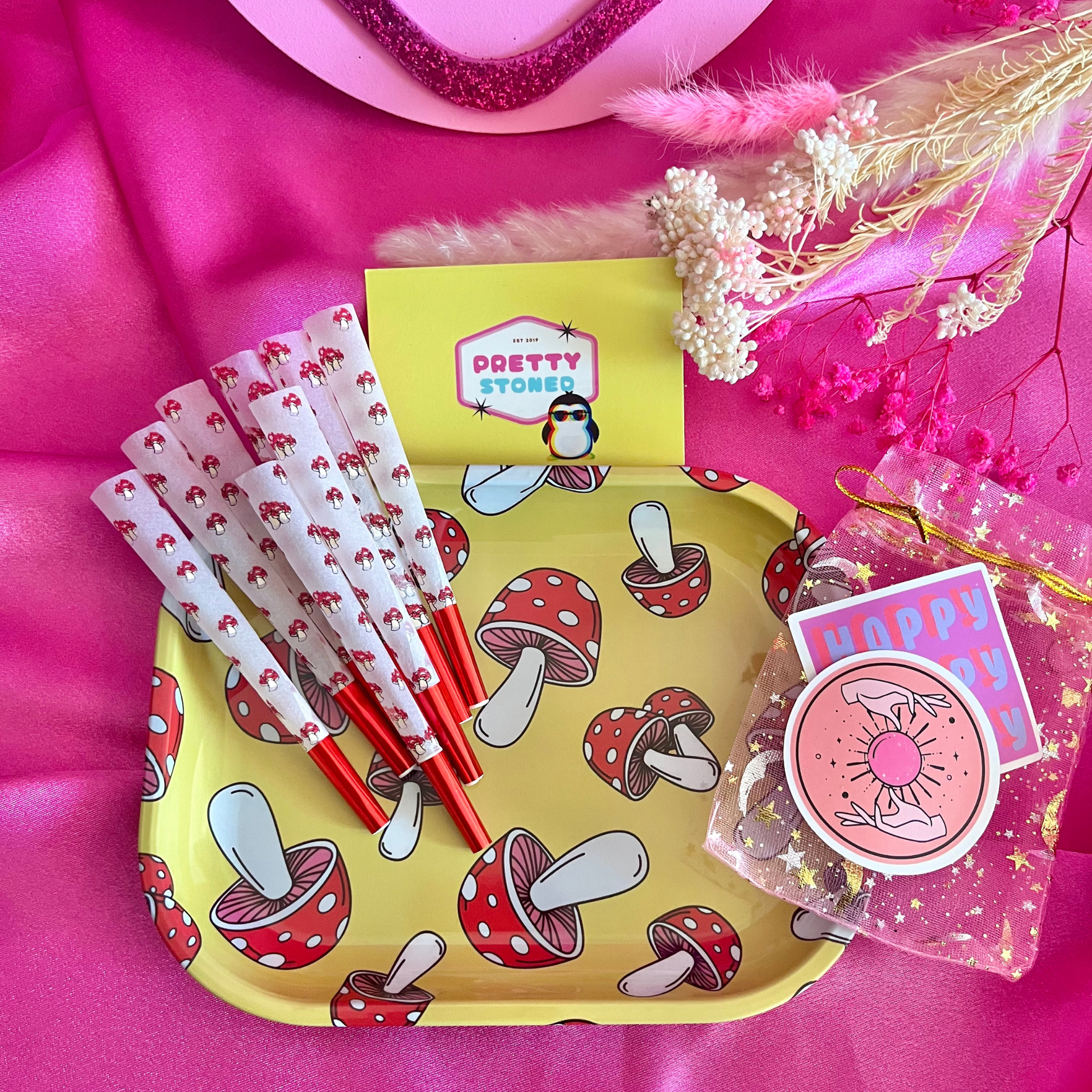 Yellow tray with mushroom design, mushroom pre rolled cones, and pink heart-shaped box on a pink background